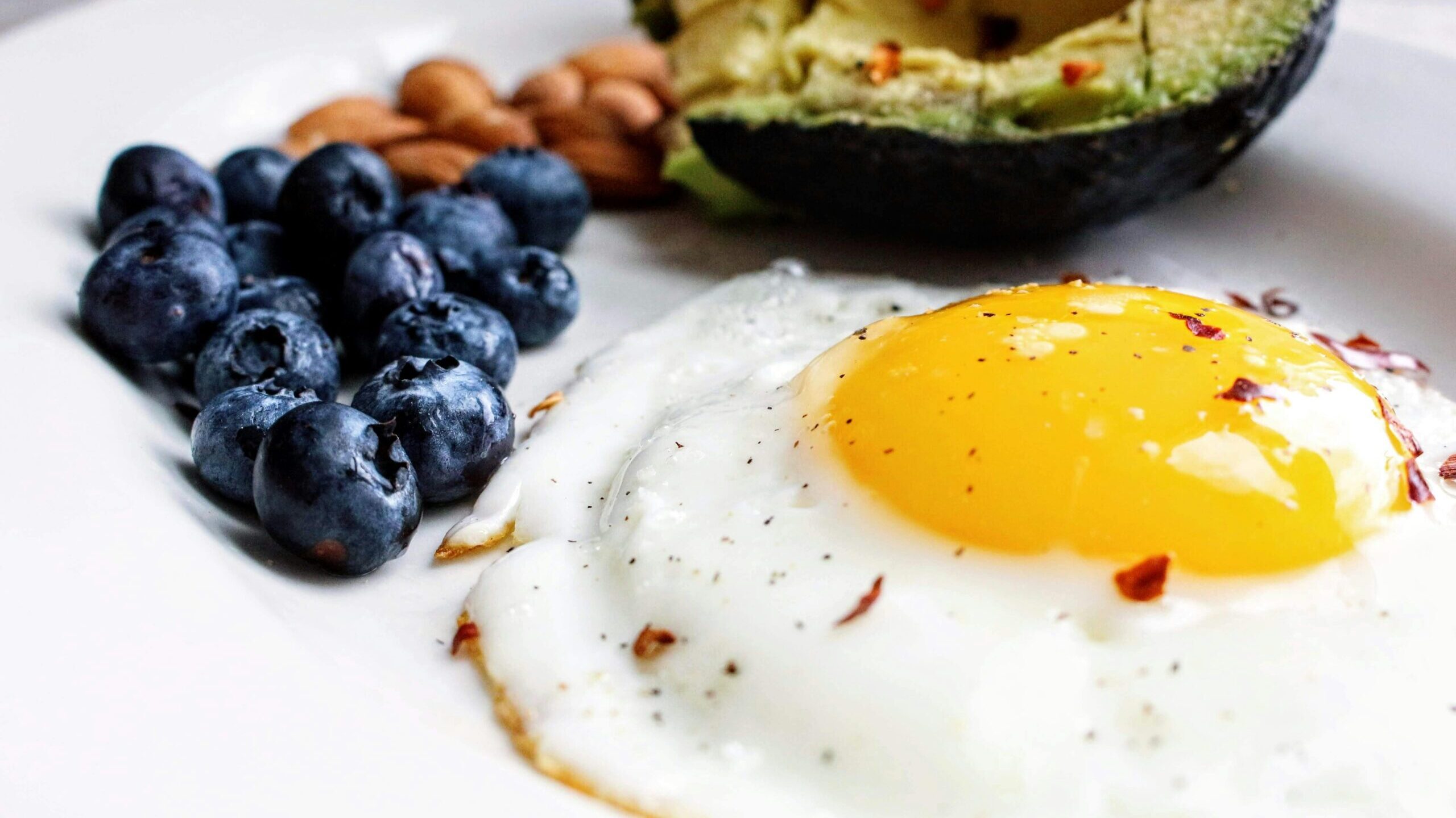 A nutritious breakfast featuring a fried egg, avocado, blueberries, and almonds.
