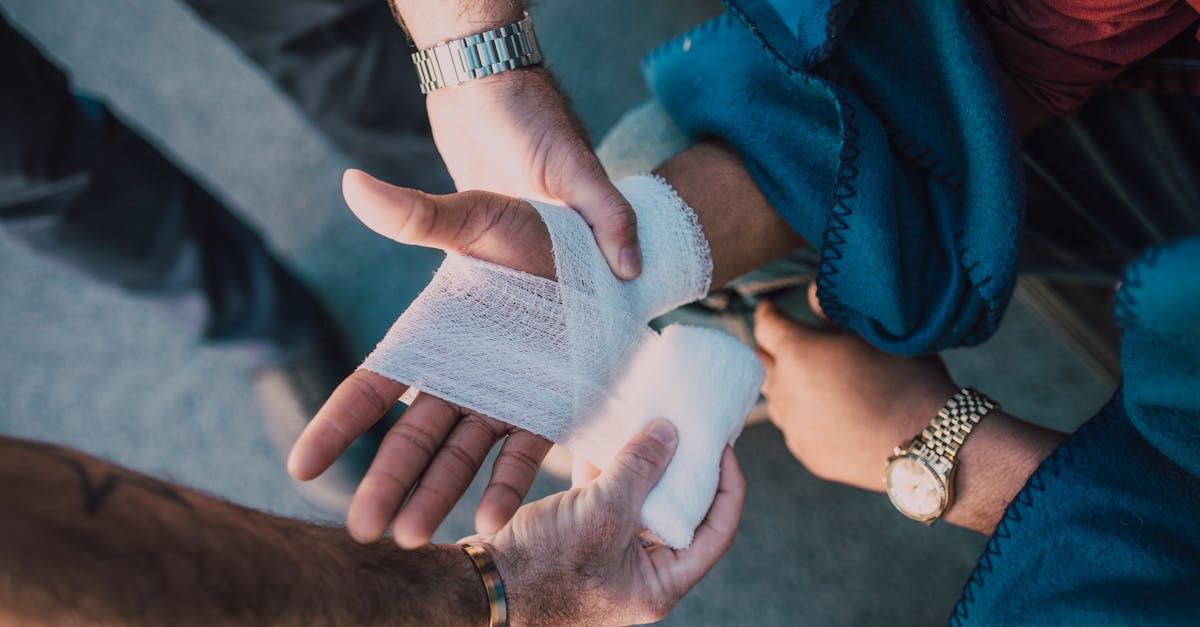 Close-up of two people bandaging an injured hand outdoors, focusing on first aid care.